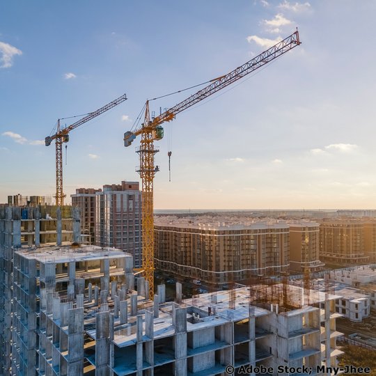 Zwei Krananlagen, die auf einer Baustelle über einem mehrstöckigen Gebäude arbeiten.