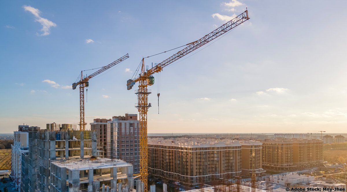 Zwei Krananlagen, die auf einer Baustelle über einem mehrstöckigen Gebäude arbeiten.